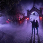 Un couple contemple un portail gothique brumeux lors d'une soirée Halloween Horror Nights.