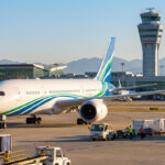Un avion Boeing 787 Dreamliner circule sur le tarmac d'un aéroport près d'une tour de contrôle par une journée ensoleillée.