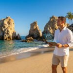 Un homme en chemise blanche sur une plage de Los Cabos tient une tablette affichant un sceau de spécialiste certifié.