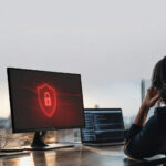 Une personne travaillant sur ordinateur face à une alerte de cybersécurité affichant un bouclier rouge avec un cadenas.