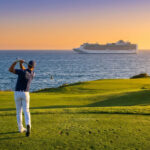 Un golfeur effectue un swing sur un terrain côtier au coucher du soleil avec un navire de croisière en arrière-plan.