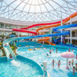 Vue intérieure d'un immense parc aquatique lumineux avec des toboggans colorés et une piscine à vagues.
