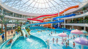 Vue intérieure d'un immense parc aquatique lumineux avec des toboggans colorés et une piscine à vagues.