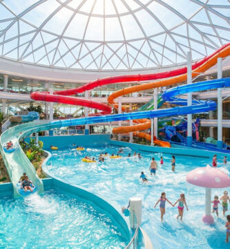 Vue intérieure d'un immense parc aquatique lumineux avec des toboggans colorés et une piscine à vagues.